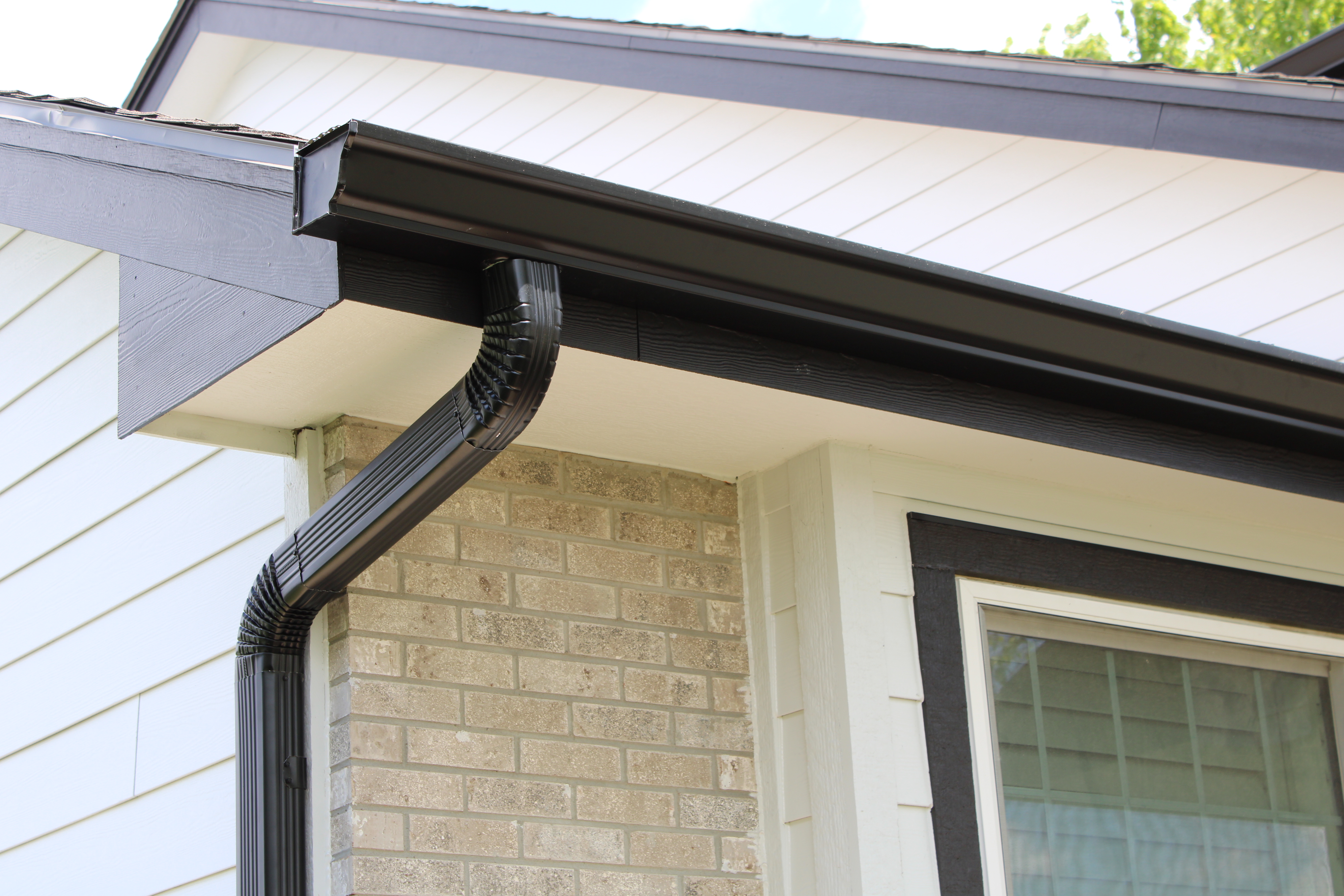 Close-up of a black seamless aluminum gutter and downspout installed on an Omaha home